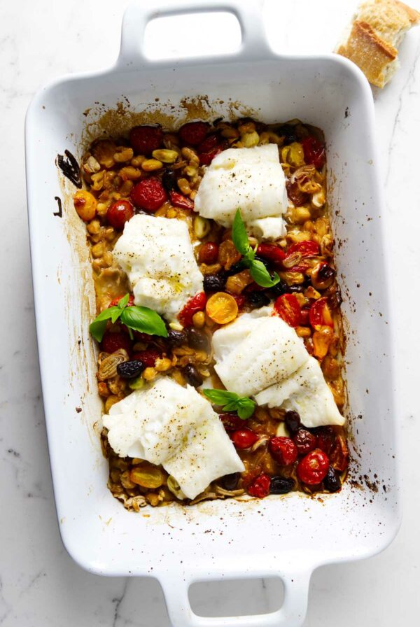 Baked cod in a ceramic dish with tomatoes, olives, and beans.