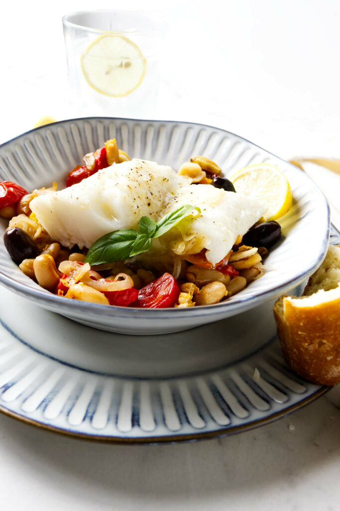 A dish filled with baked cod, beans, and roasted tomatoes.