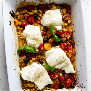 A baking dish filled with roasted cod on tomatoes, beans, and olives.