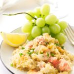 Seafood mac n cheese with parsley, lemon wedge, green grapes, and a fork.