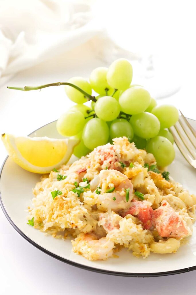 Seafood mac n cheese with parsley, lemon wedge, green grapes, and a fork.