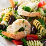 Pasta salad with shrimp, peppers, olives, and cucumber on a white plate.