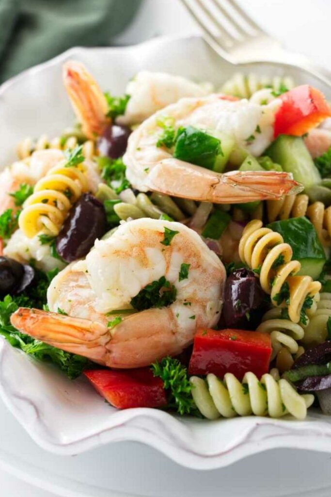 Pasta salad with shrimp, peppers, olives, and cucumber on a white plate.