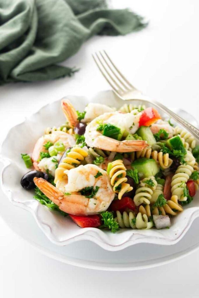 Cold shrimp pasta salad with vegetables, and olives on a white plate with fork.