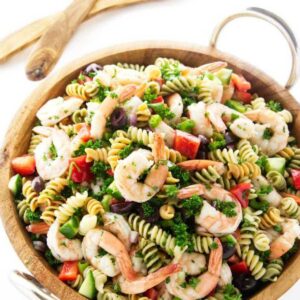 Wooden bowl of pasta salad with shrimp and vegetables.