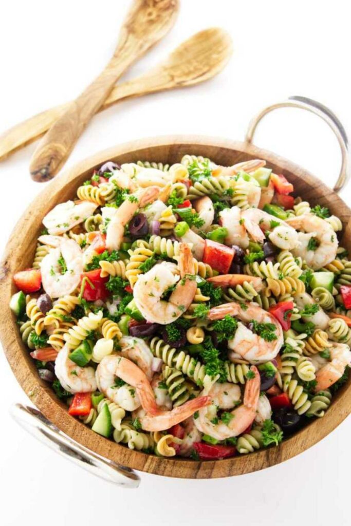 Wooden bowl of pasta salad with shrimp and vegetables.