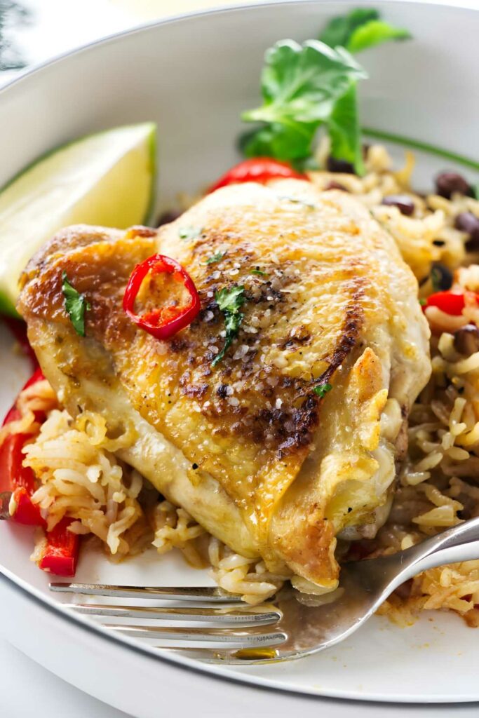 Baked chicken thigh on rice with beans, peppers, chili, herbs, and lime.