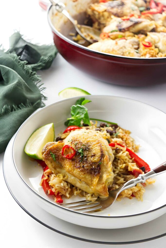 Seasoned chicken on rice with peppers, herbs, lime wedge, and sliced chili.