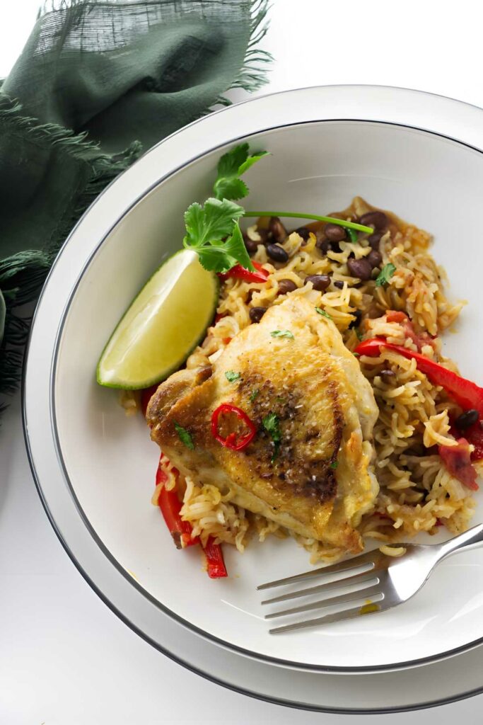 Cooked chicken atop seasoned rice with beans, peppers, lime, and cilantro.