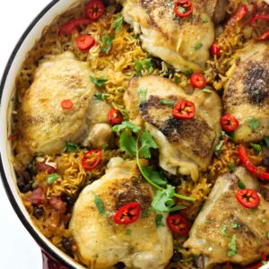 Golden-brown chicken thighs on rice in a red Dutch oven, garnished with chili and cilantro.