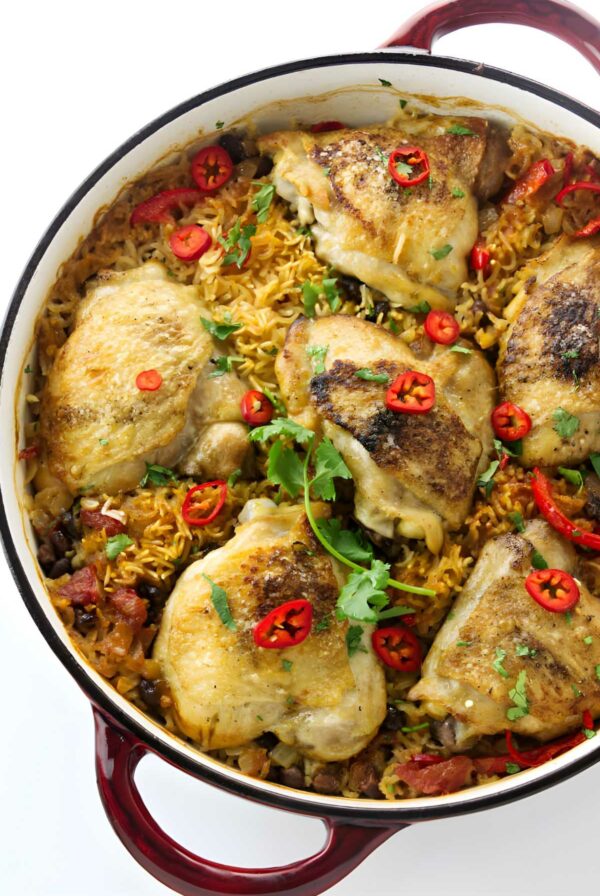 Golden-brown chicken thighs on rice in a red Dutch oven, garnished with chili and cilantro.