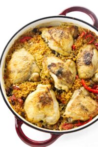 Baked chicken thighs on golden rice with red peppers in a red Dutch oven.