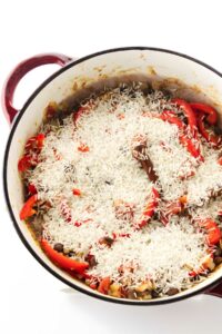 Red pot with uncooked rice, peppers, beans, and vegetables seen from above.