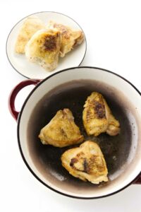 Round pot with three browned chicken thighs, plate with two more nearby.
