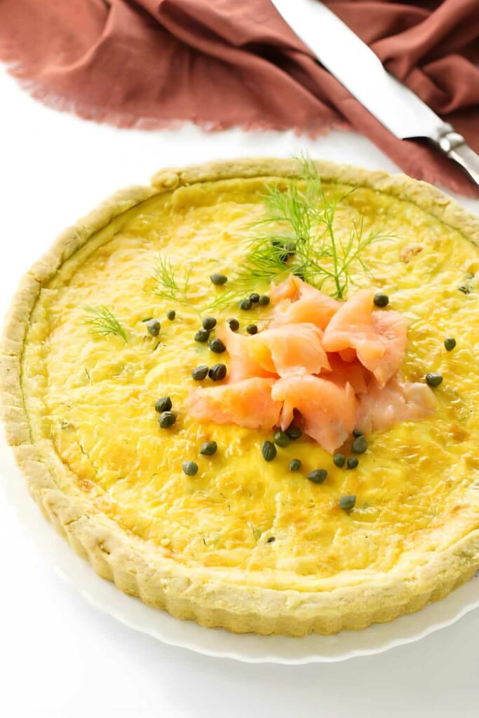 Quiche with smoked salmon, capers, and dill on a white plate.