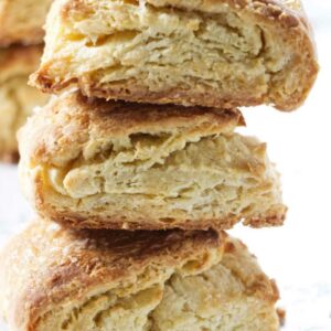 Stack of three golden-brown, flaky scones against a light background.