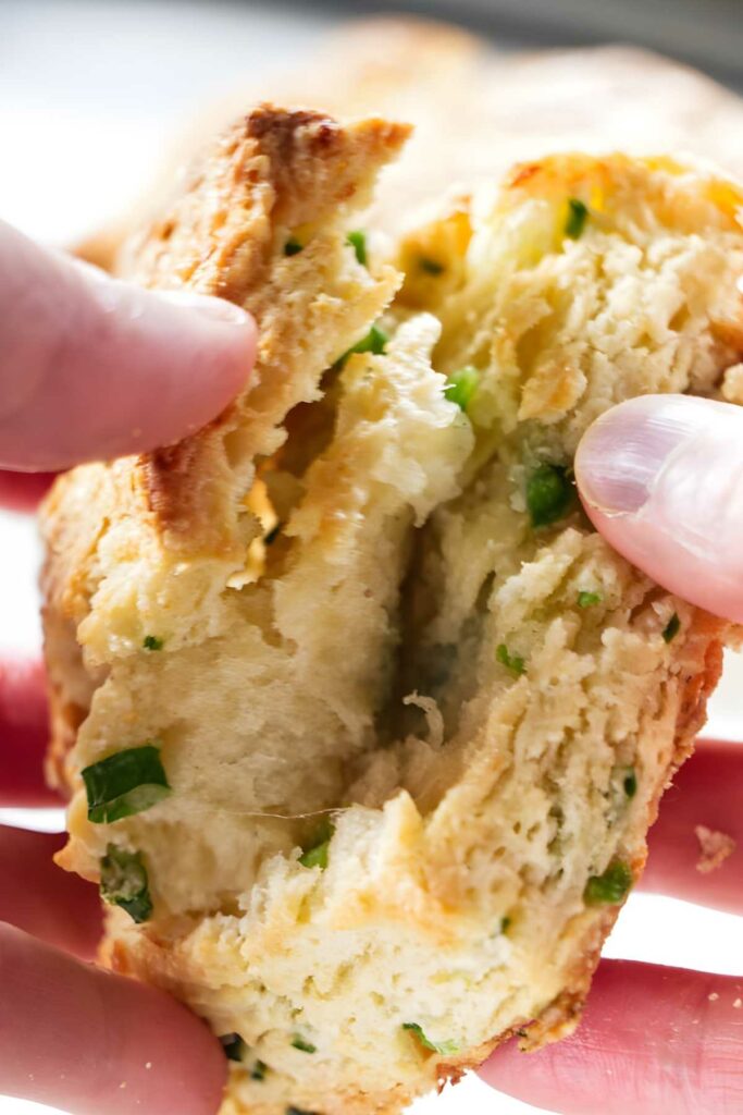 Hands break open a flaky biscuit with green onions. 