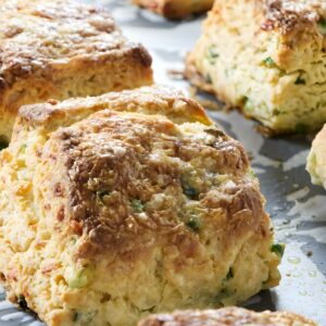 Golden-brown square scones with green herbs on a parchment-lined baking sheet.