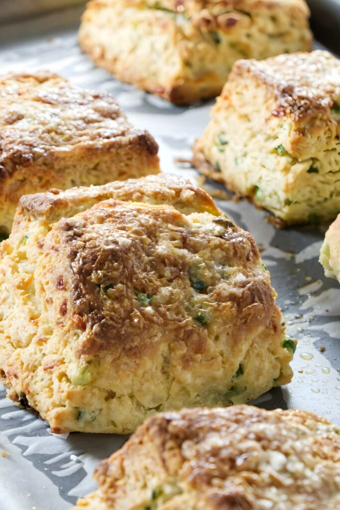 Golden-brown cheesy biscuits with green onions on a parchment.