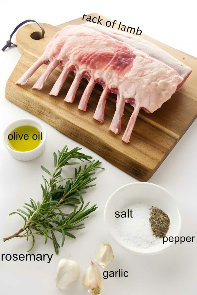 Raw rack of lamb on board, surrounded by labeled seasoning dishes and rosemary.