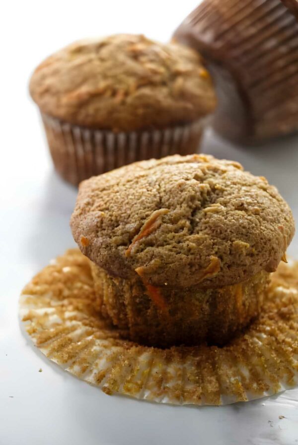 Close-up of a muffin with crinkled liner, two muffins behind on white.