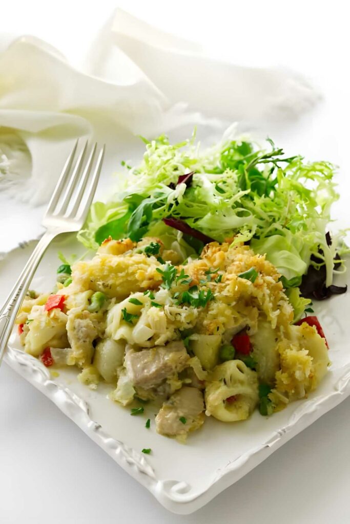 Cheesy tuna pasta bake with herbs and salad on a white plate.