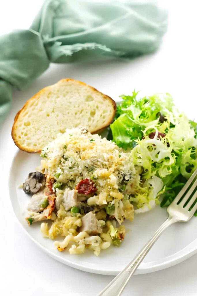 Turkey casserole with breadcrumbs, bread slice, and salad on a white plate.