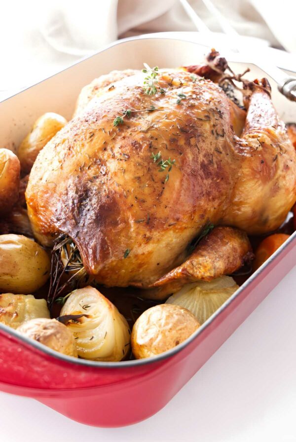 Roasted chicken with herbs in red dish, potatoes and onions.