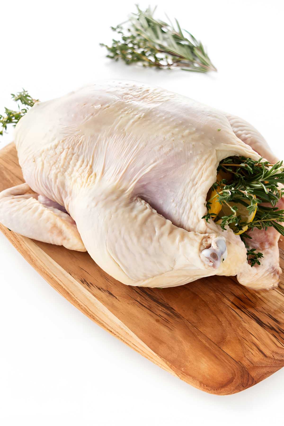 Raw chicken stuffed with herbs and lemon on a wooden cutting board.