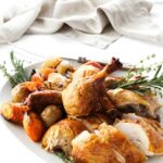 Roasted chicken with crispy skin, potatoes, carrots, and herbs on a plate.