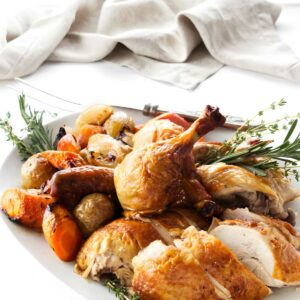 Roasted chicken with crispy skin, potatoes, carrots, and herbs on a plate.