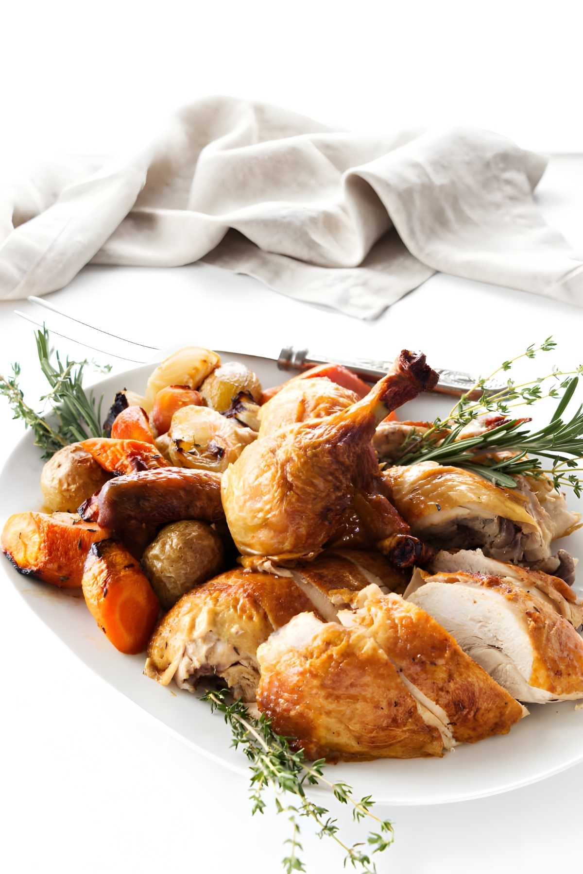Roasted chicken with crispy skin, potatoes, carrots, and herbs on a plate.