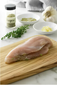 Adding herbs and seasoning to a chicken breast.