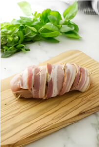 Wrapping a chicken breast in bacon.