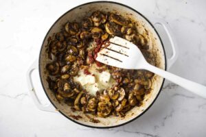 Adding butter and tomato paste to sauteed mushrooms.