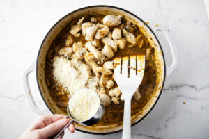 Adding parmesan cheese to the chicken and marsala sauce.