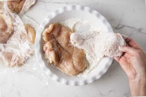 Dredging chicken in flour.