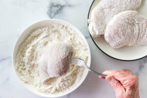 Dredging chicken in flour.