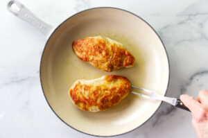 Searing chicken breasts in a skillet.