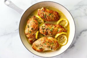 Browned chicken in a skillet with lemon piccata sauce.