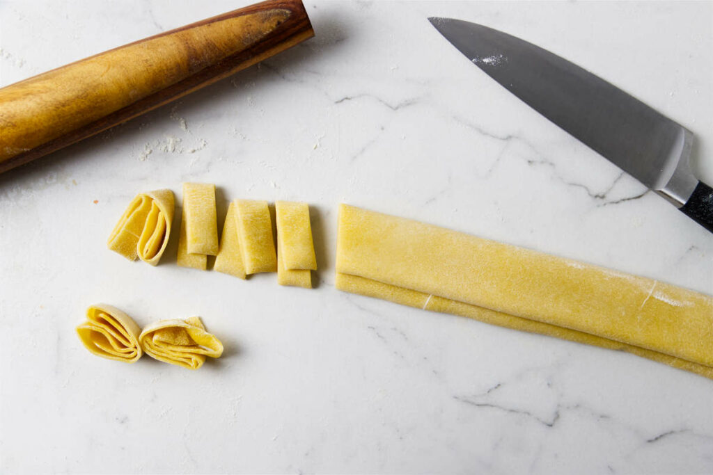 Slicing strips of fresh pasta with a knife.