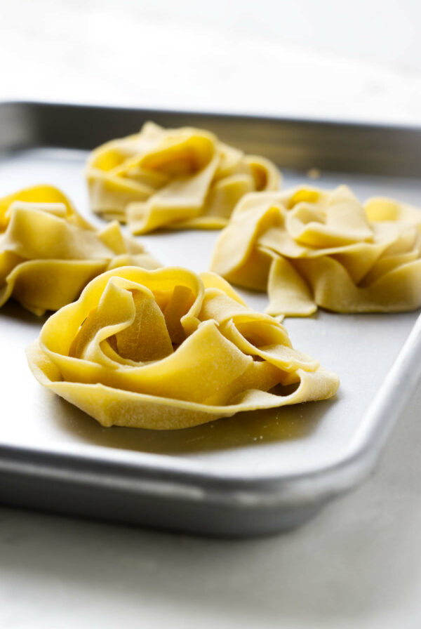 Piles of homemade einkorn pasta drying on a sheet pan.