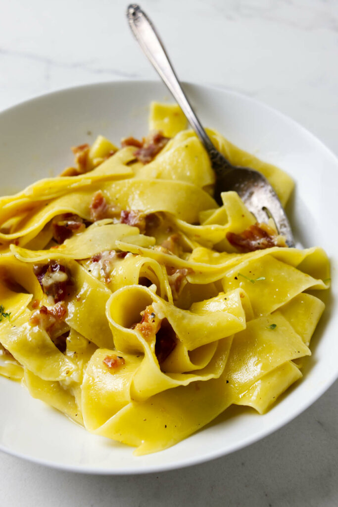 Wide pasta noodles made from einkorn flour in a pasta bowl with bacon.