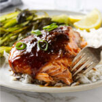 A fork flaking a piece of garlic ginger soy salmon on a bed of rice.
