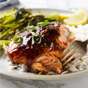 A fork flaking a piece of garlic ginger soy salmon on a bed of rice.