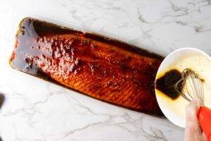 Pouring a marinade over a side of salmon.