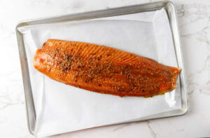 A whole salmon fillet on a baking sheet with parchment paper.