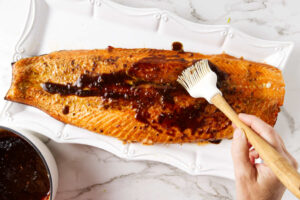 Brushing marinade over the top of a whole side of salmon.