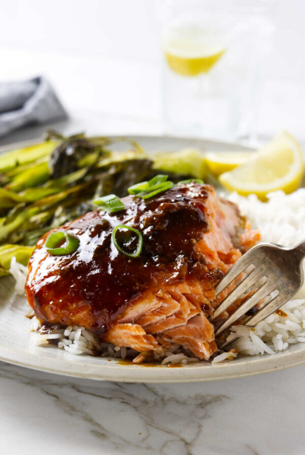 A fork flaking off a piece of garlic soy salmon on a dinner plate.