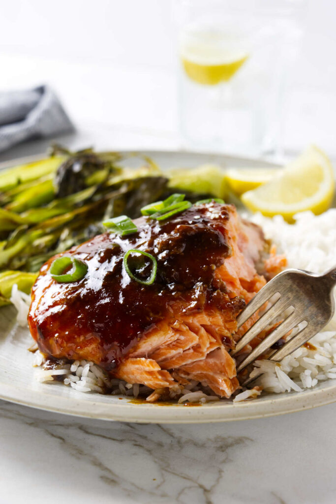 A fork flaking off a piece of garlic soy salmon on a dinner plate.